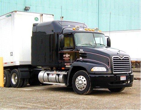 A black semi-truck with a white trailer is parked on a concrete surface. The Star Extruded Shapes logo marks the truck with orange lights on top, with an industrial building in the background.