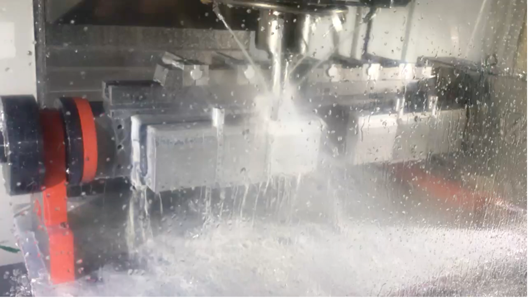 Snapshot of the CNC machine in action. An aluminum piece is mounted inside and able to rotate 360 degrees so that the cutting mechanism can remove portions to achieve the desired shapes from the aluminum. Water is constantly being sprayed during to process to cut down on friction and heat.