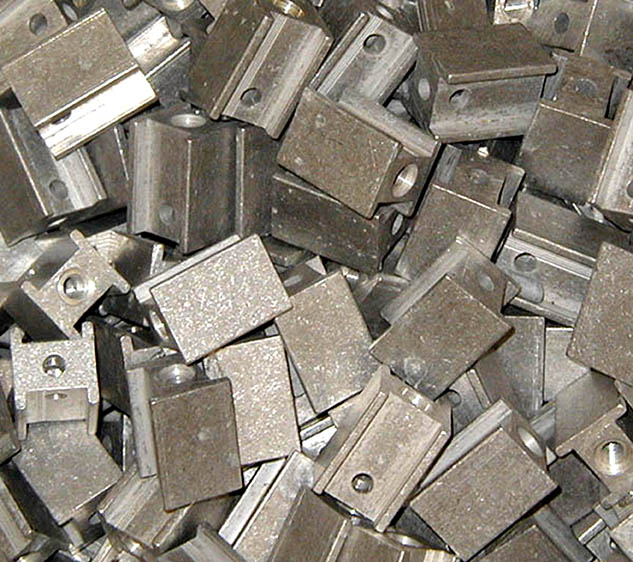 Shiny Aluminum parts that are punched and tumble deburred, piled on one another haphazardly.